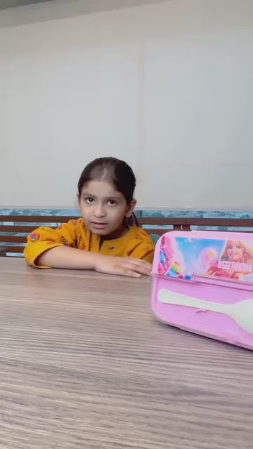 Musfira Bilal, the CEO of Bentokids, a young girl with a bright smile, sitting at a wooden table in an orange shirt. A pink Bentokids lunchbox with a doll graphic is visible on the right. Is this video where Musfira Bilal is describing the features of the Bentokids product